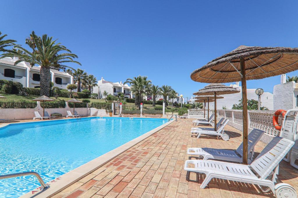 a swimming pool with chairs and an umbrella at Vila Mourisca in Armação de Pêra