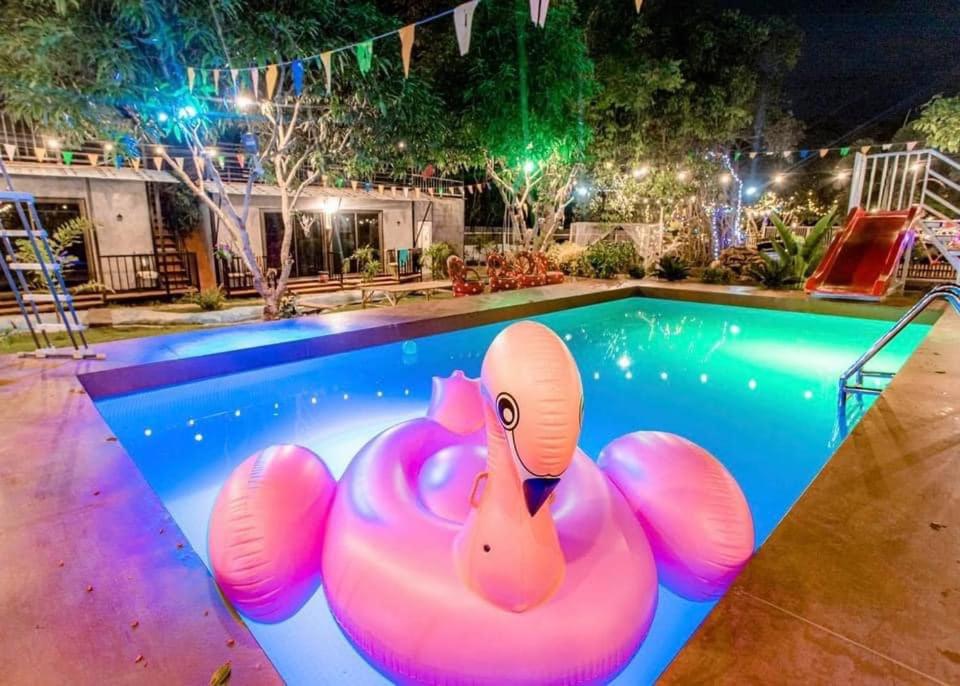 una piscina con un cisne rosa en el agua por la noche en บ้านอบอุ่น By The Mountain Ozoneบ้านโอโซนขุนเขาแก่งกระจาน en Ban Song Phi Nong