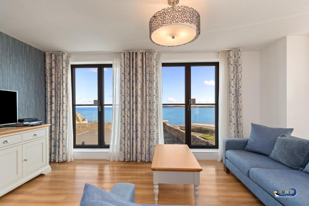 a living room with a blue couch and windows at Apartment 8 Waterstone House - Luxury Apartment, Sea Views, Pet Friendly in Tenby