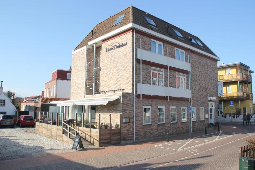 een groot bakstenen gebouw op een straat met auto's geparkeerd voor bij Hotel Duinlust in Domburg