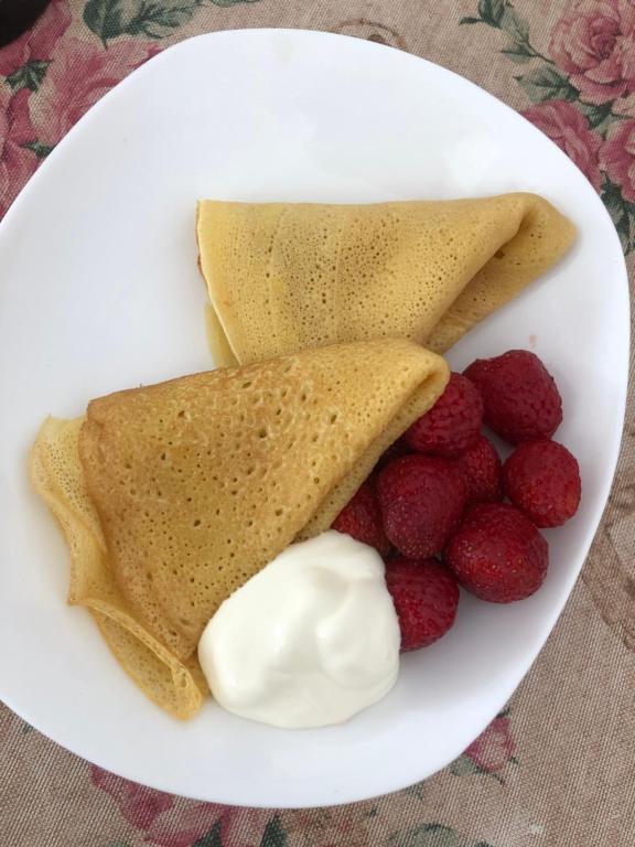 a white plate with pancakes and raspberries and whipped cream at Family Guest House in Cholpon-Ata