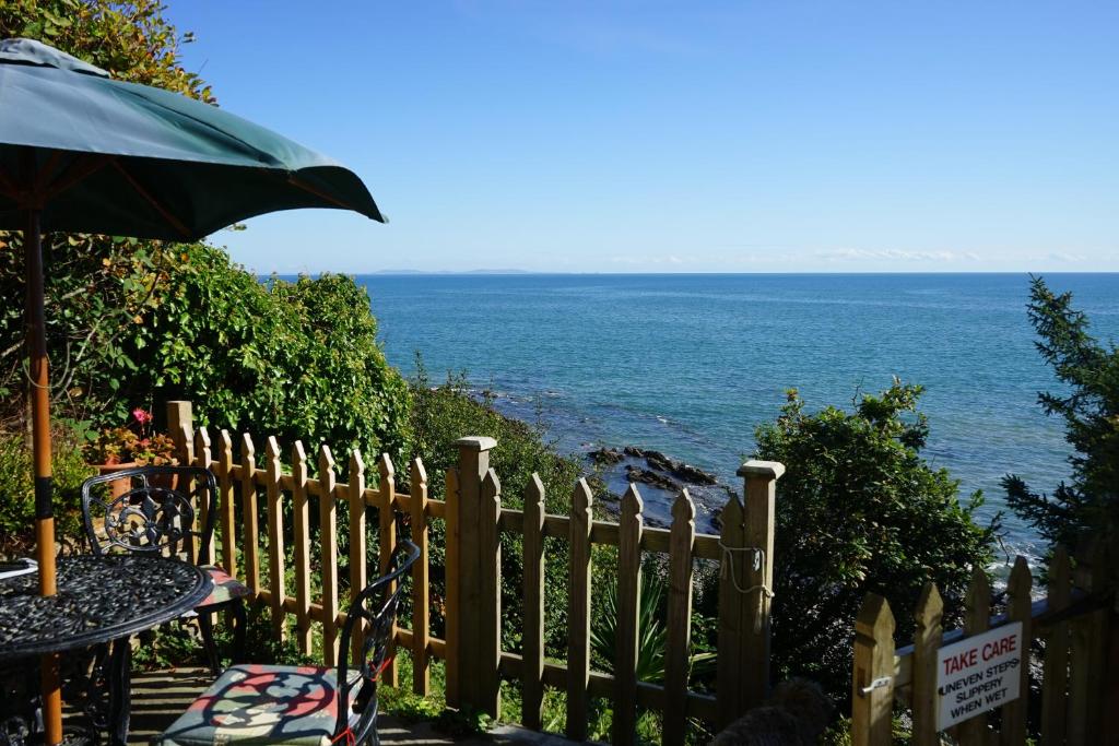 a table with an umbrella next to the ocean at The Cottage - Sea Views, Direct Access to Beach, Pet Friendly in Stepaside