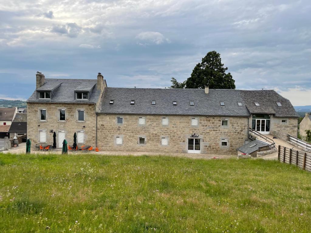 un gran edificio de ladrillo con un campo de hierba delante de él en La ferme de l'Aubrac en Aumont-Aubrac