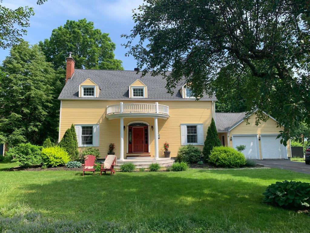 uma casa amarela com duas cadeiras no quintal em Manoir Alegria em Cowansville