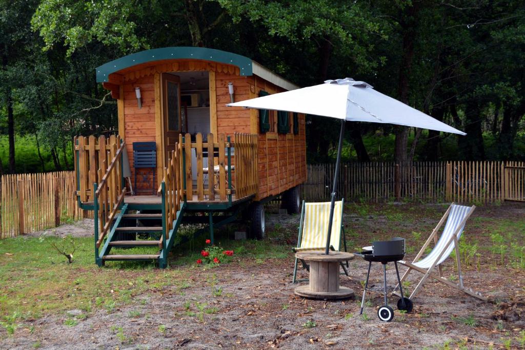 una casetta con due sedie e un ombrellone di Roulotte paisible au milieu de la nature a Sainte-Eulalie-en-Born