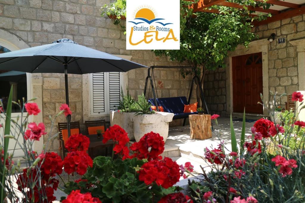 eine Terrasse mit roten Blumen und einem Sonnenschirm in der Unterkunft Studio Apartments & Rooms Lela in Šipanska Luka