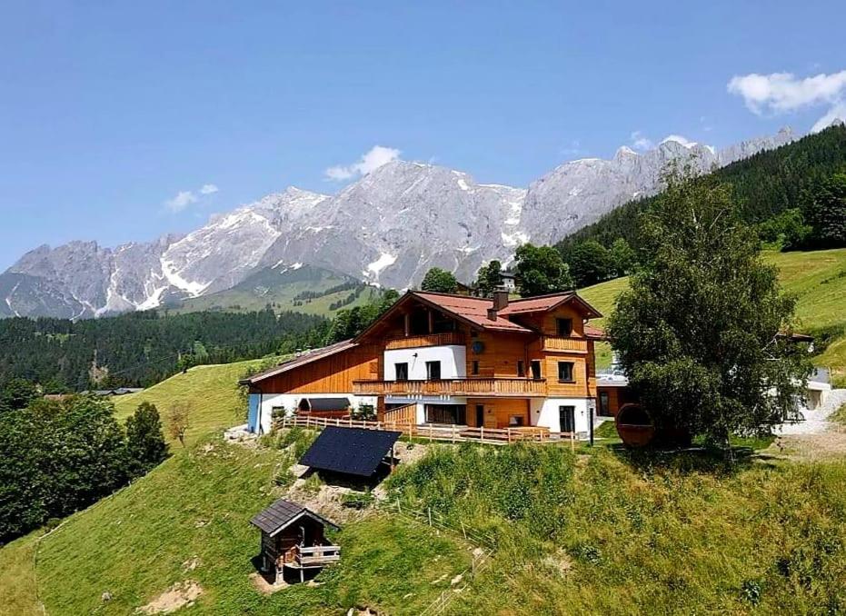 una casa en una colina con montañas en el fondo en Gut Stein Panoramalodge, en Mühlbach am Hochkönig
