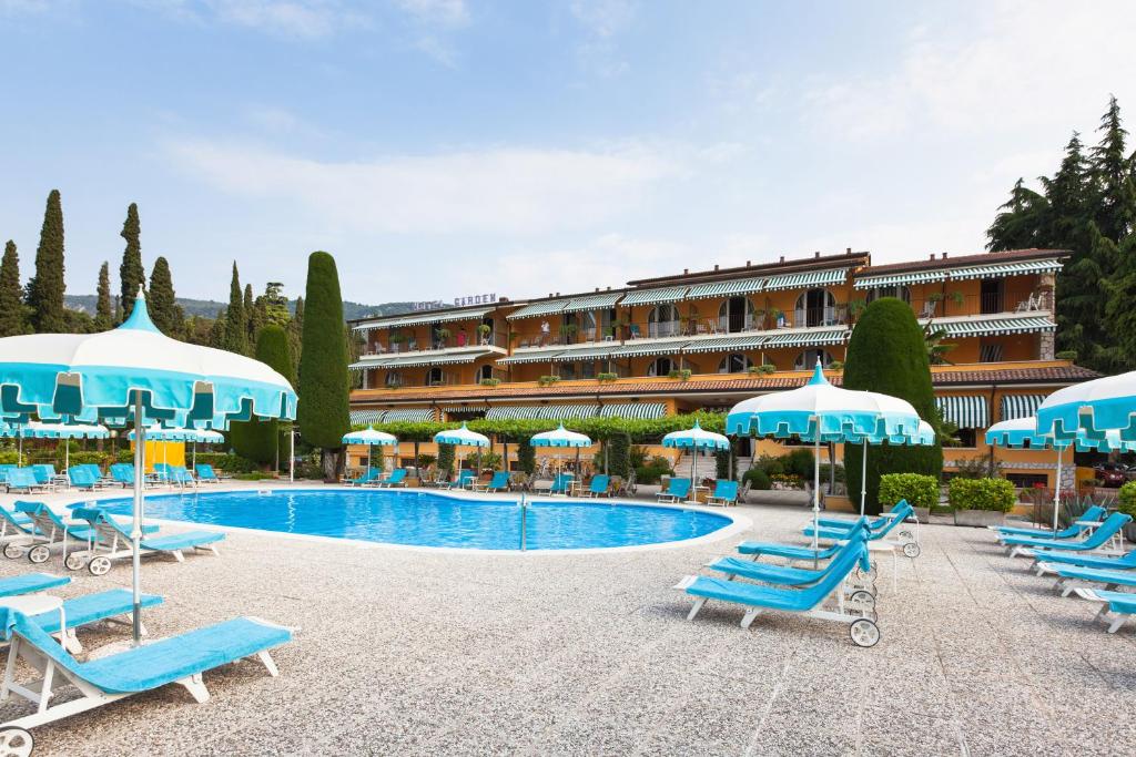 un hotel con una piscina con sillas azules y sombrillas en Hotel Garden, en Garda