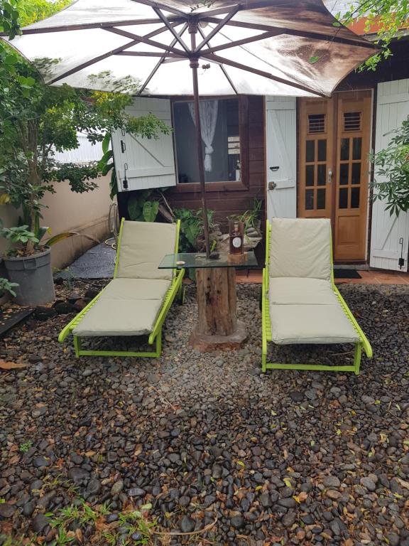 eine Terrasse mit 2 Stühlen, einem Tisch und einem Sonnenschirm in der Unterkunft Le Laurier Rose in Basse-Terre