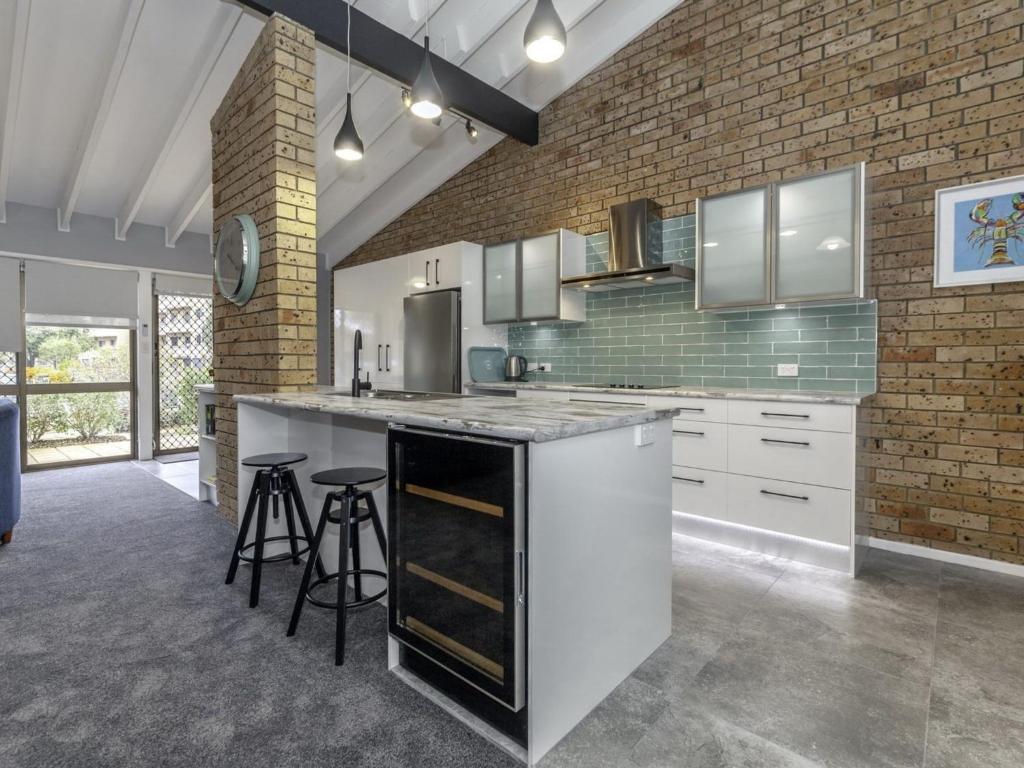 a kitchen with white cabinets and a brick wall at Bay Parklands 4, 2 Gowrie Avenue - pool & tennis court in Nelson Bay