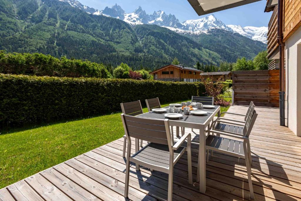 una mesa y sillas en una terraza de madera con montañas en La Cordee 703 Apartment - Chamonix All Year, en Chamonix-Mont-Blanc
