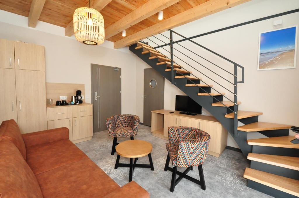 Cozy duplex living area with brown sofa, patterned armchairs, wooden staircase, small coffee table, TV console.