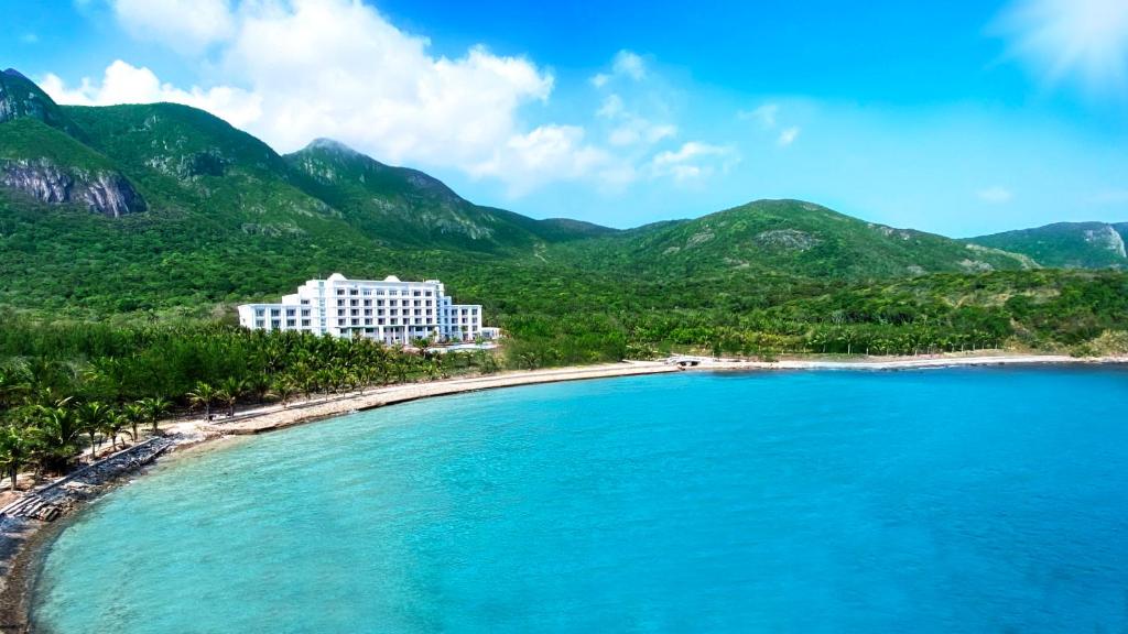 a hotel on a beach with mountains in the background at Orson Hotel & Resort Con Dao in Con Dao