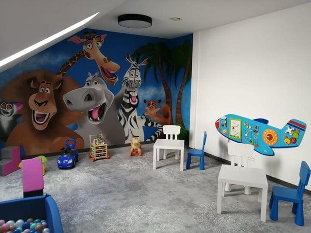 Children's playroom with large cartoon animal mural, small tables and chairs, assorted floor toys and ball pit.
