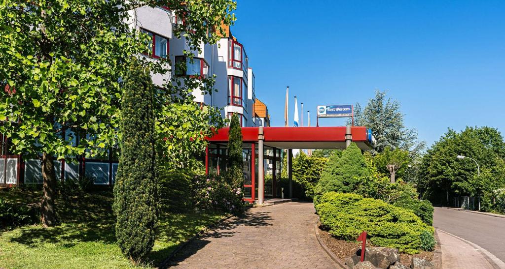 un bâtiment avec un auvent rouge à côté d'une rue dans l'établissement Best Western Victor's Residenz-Hotel Rodenhof, à Sarrebruck