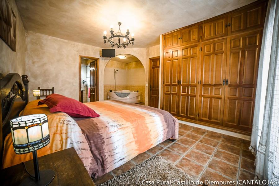 a bedroom with a large bed and a bathroom at Casa Rural Castillo Diempures in Cantalojas