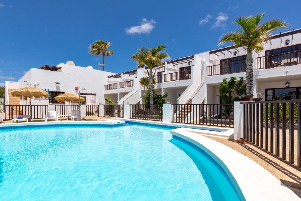 a swimming pool in front of a building with palm trees at Apartamentos las Lilas in Puerto del Carmen