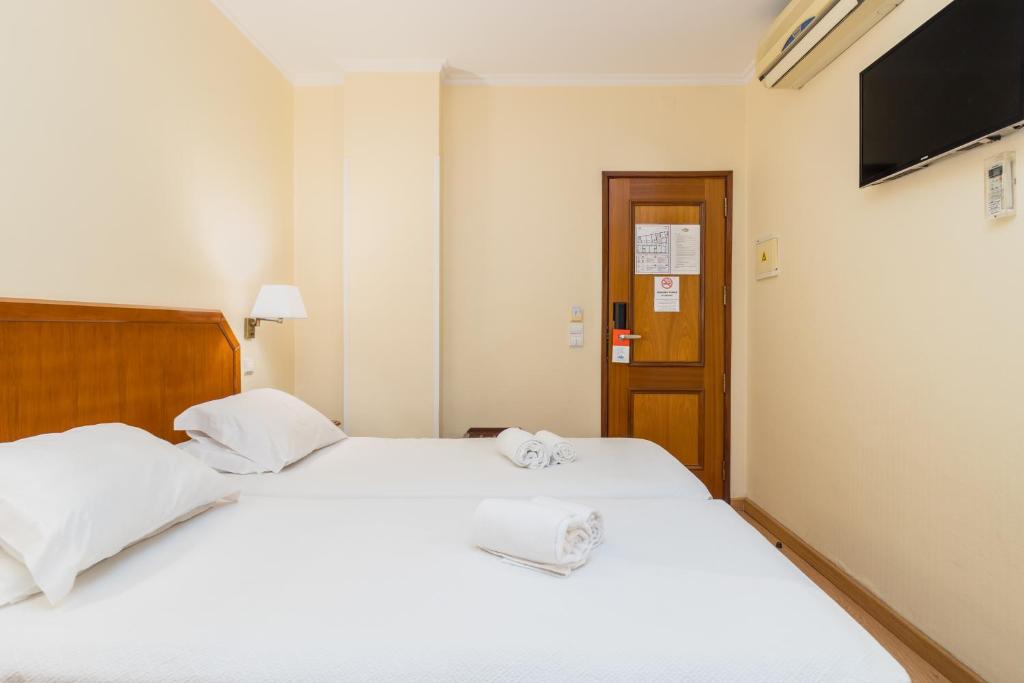 a bedroom with two beds with white sheets and a television at Hotel Residencial Colibri in Costa da Caparica