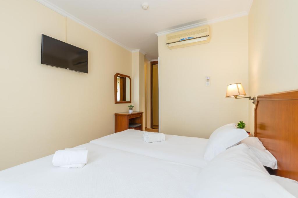a bedroom with two beds and a tv on the wall at Hotel Residencial Colibri in Costa da Caparica