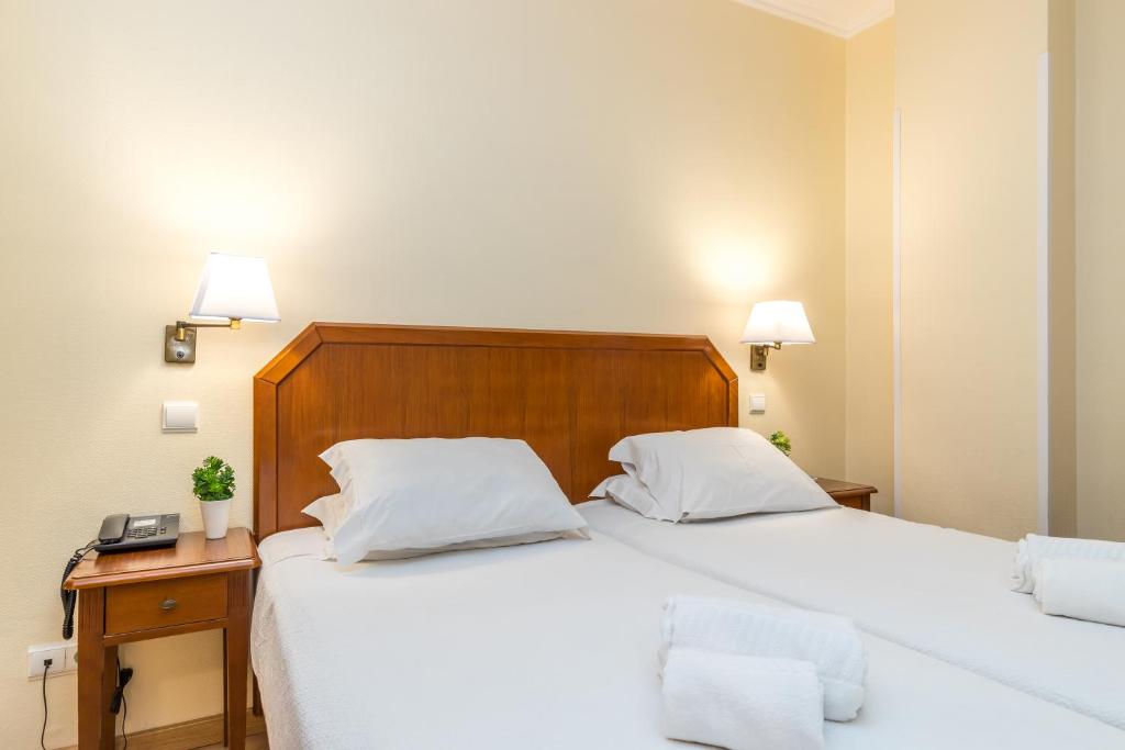 a bedroom with two beds with white sheets and a wooden headboard at Hotel Residencial Colibri in Costa da Caparica