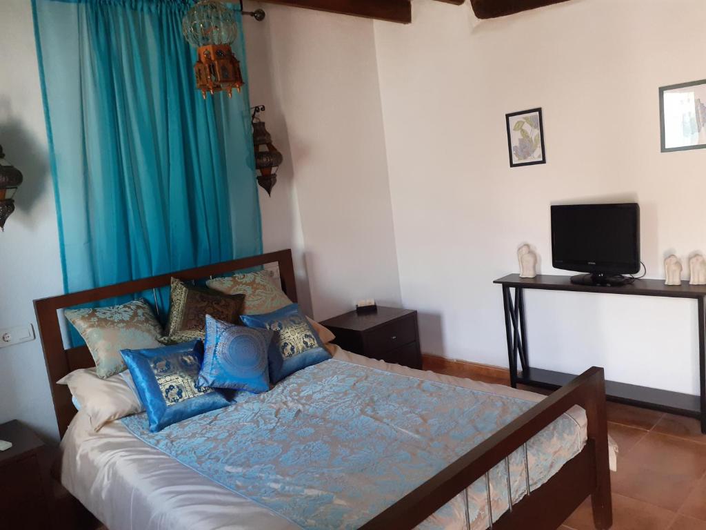 a bedroom with a bed with blue pillows and a television at Casita Adela in Huéscar