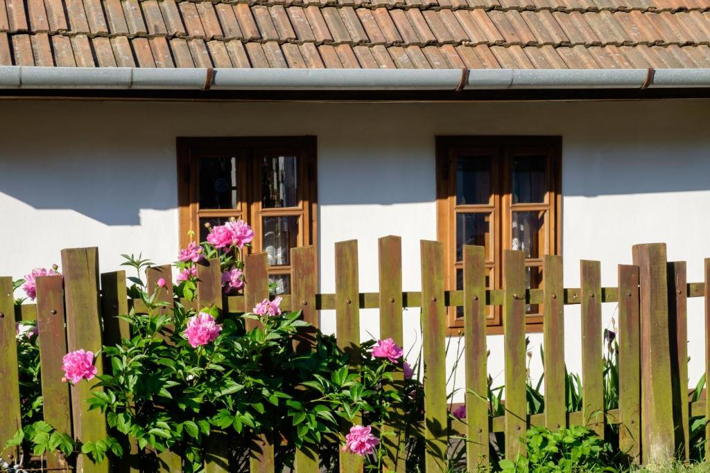 a wooden fence in front of a house with pink flowers at Lóci Palócház in Nagylóc