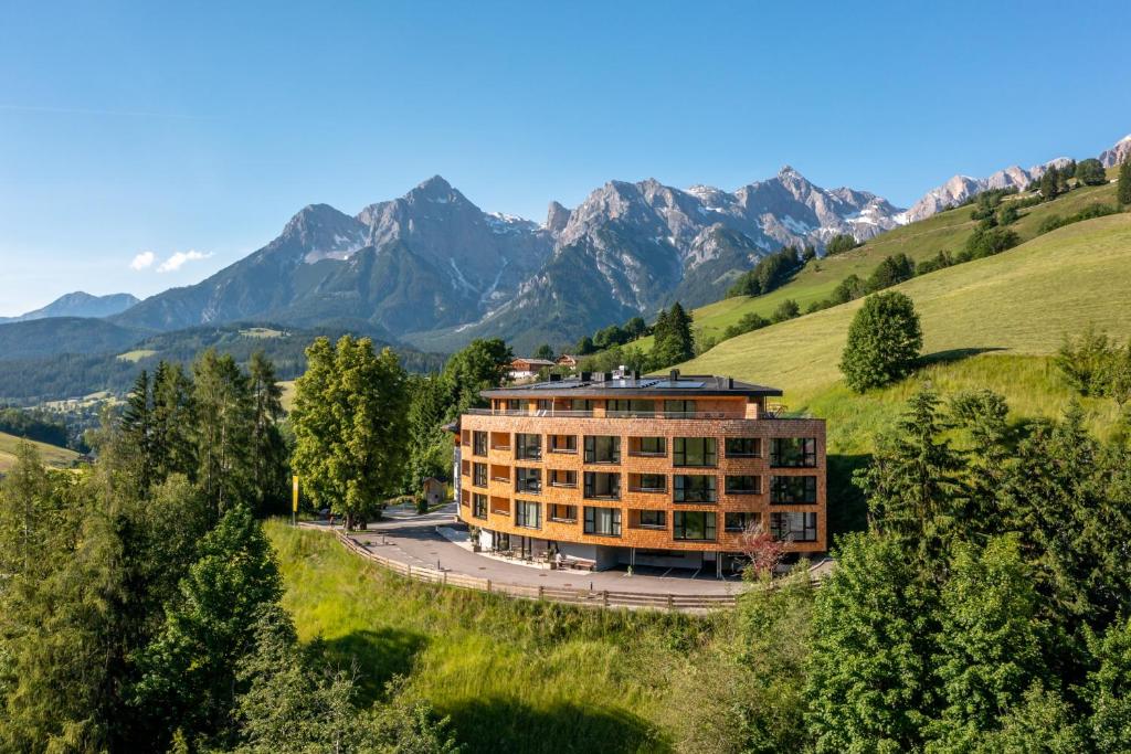 a building on a hill with mountains in the background at Apartmenthotel Sonnenhof in Maria Alm am Steinernen Meer
