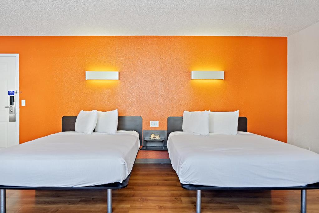 two beds in a room with an orange wall at Carlsbad Village Inn in Carlsbad