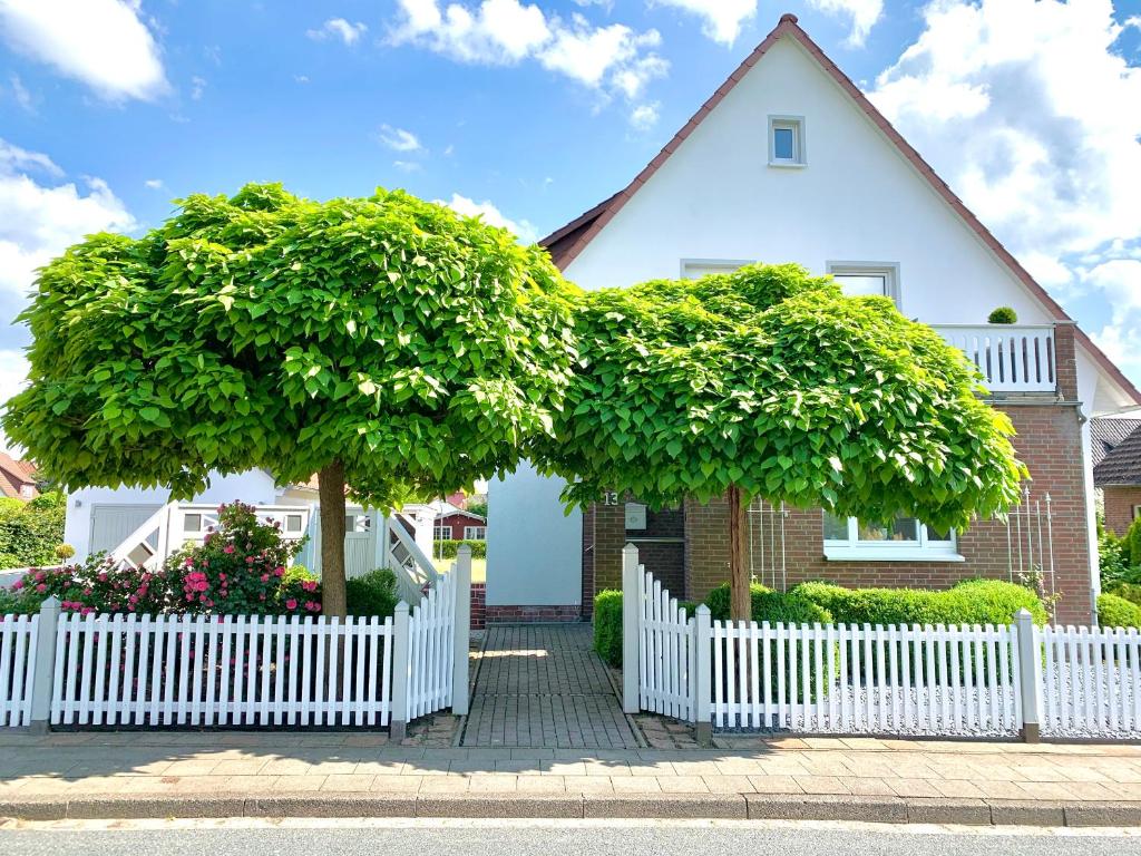 una cerca blanca frente a una casa con un árbol grande en Ferienwohnung HeideZeit Soltau - Neu mit Spielturm en Soltau