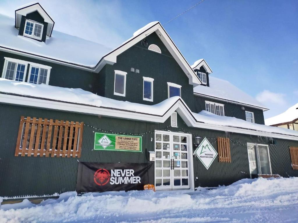 une maison noire avec de la neige devant elle dans l'établissement Madarao Mountain Lodge, à Iiyama