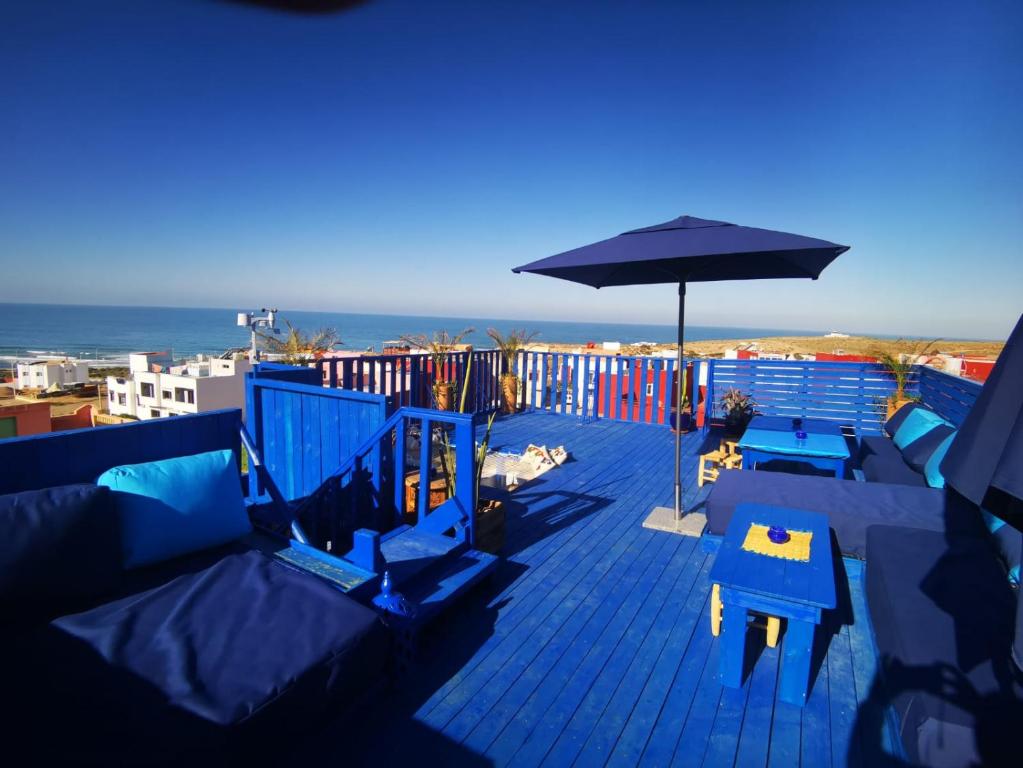 a blue deck with an umbrella and tables and the ocean at Tigmi Blue - Imsouane Surf et Océan in Imsouane