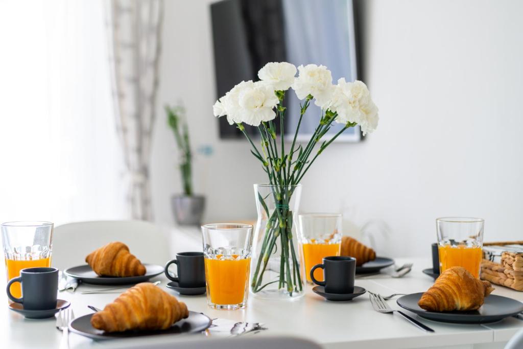 a table with a vase of white flowers and orange juice at Captain’s Home Kenese Apartman in Balatonkenese