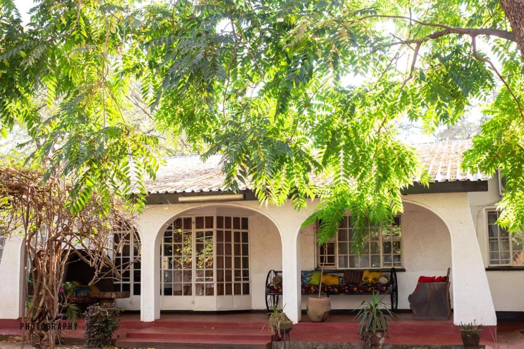 ein weißes Haus mit einer Veranda und Bäumen in der Unterkunft The Ad Lib Executive lodge in Lilongwe