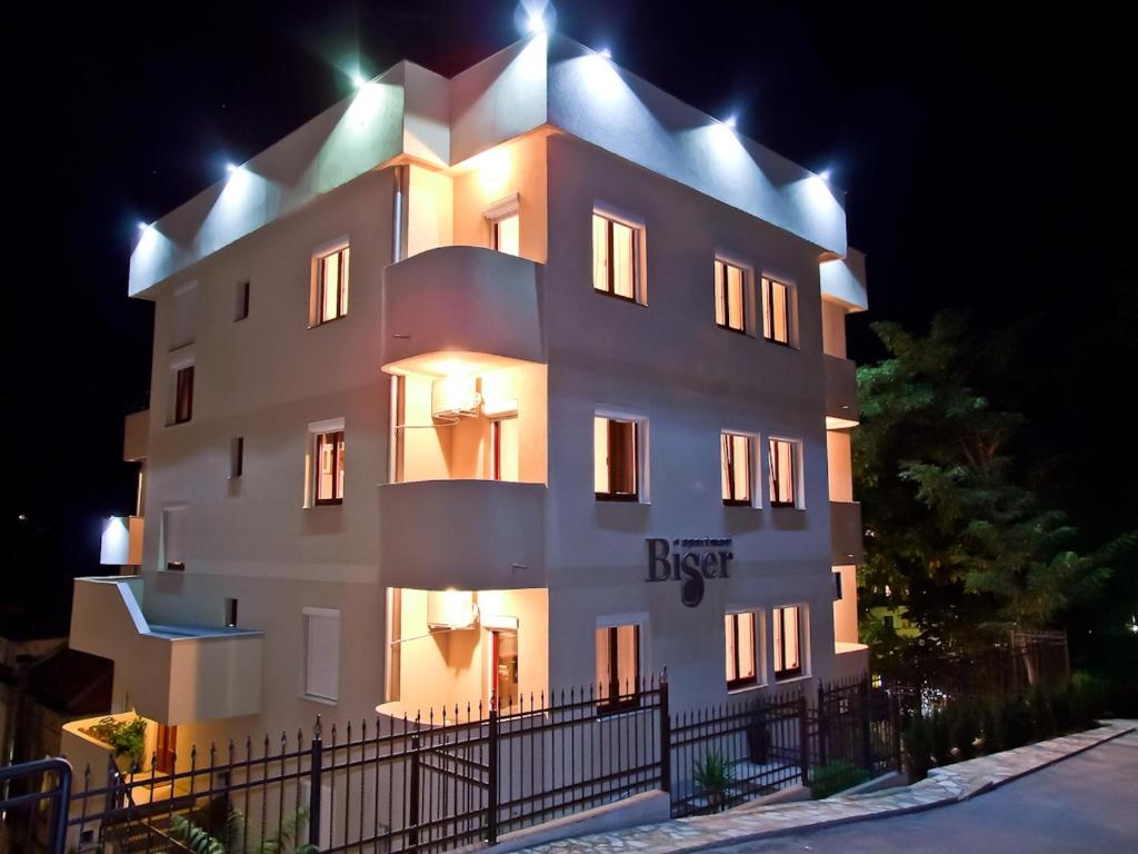 Un grand bâtiment blanc avec des lumières allumées la nuit dans l'établissement Apartments Biser, à Vrnjačka Banja