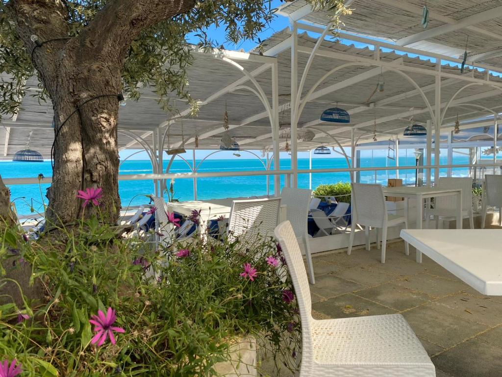 eine Terrasse mit weißen Stühlen, Tischen und einem Baum in der Unterkunft B&B direttamente sul mare da Antonino in Mattinata