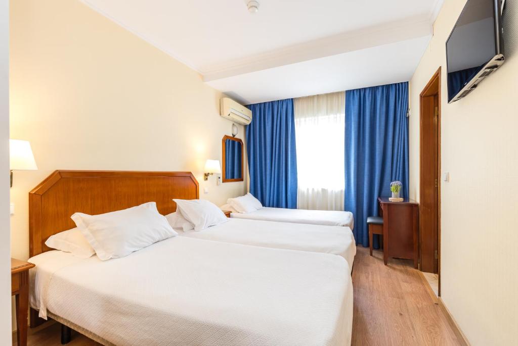 two beds in a hotel room with blue curtains at Hotel Residencial Colibri in Costa da Caparica