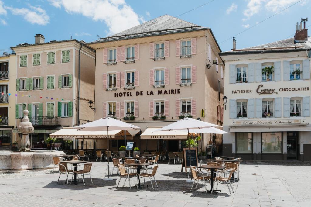 an outdoor cafe with tables and umbrellas in front of buildings at Logis - Hotel De La Mairie in Embrun