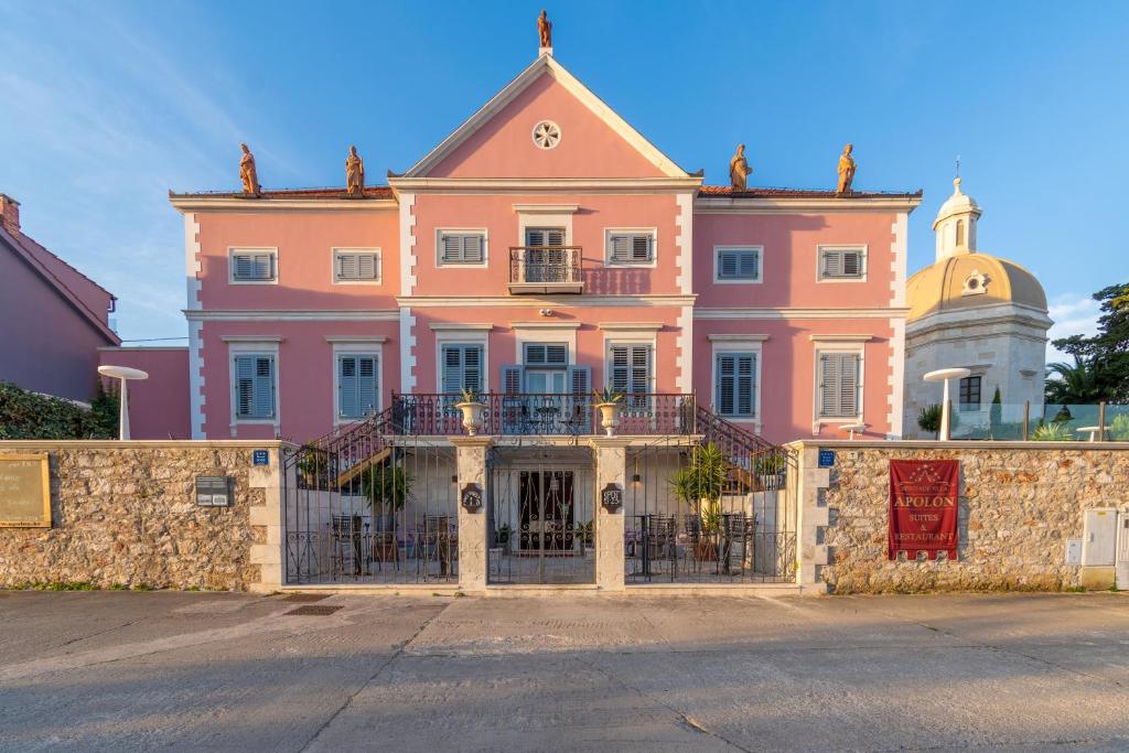 Um edifício cor-de-rosa com uma vedação à frente. em B&B Heritage Villa Apolon em Stari Grad