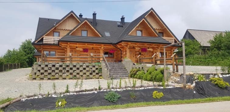 Une grande maison en bois avec des escaliers se trouve juste devant. dans l'établissement Dwór Pan Tadeusz, à Orawka