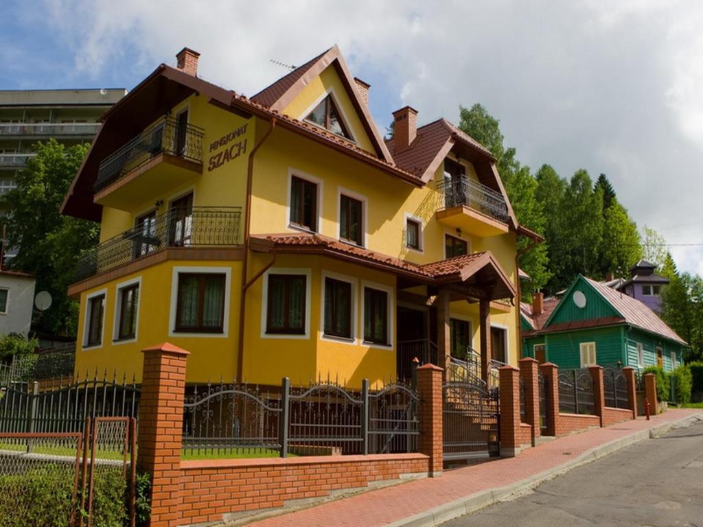 a yellow house with a brown roof at Pensjonat Szach in Krynica Zdrój