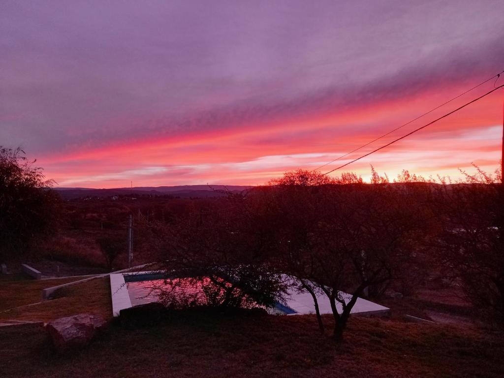 una puesta de sol sobre un campo con un árbol en primer plano en Bº CERRADO LOMAS DEL REY MAYU SUMAJ en San Antonio de Arredondo