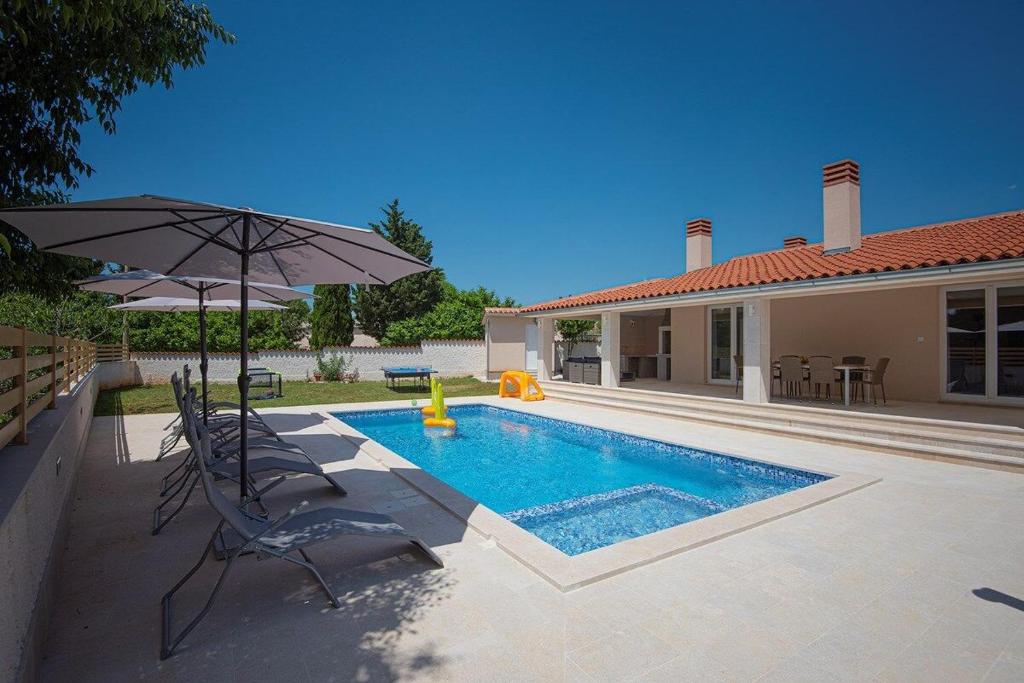 a swimming pool with an umbrella and a house at Villa Lu in Vodnjan