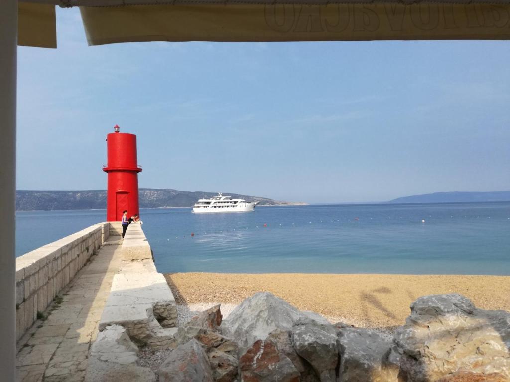 un faro rojo en la playa con un barco en el agua en Guesthouse Romana en Cres