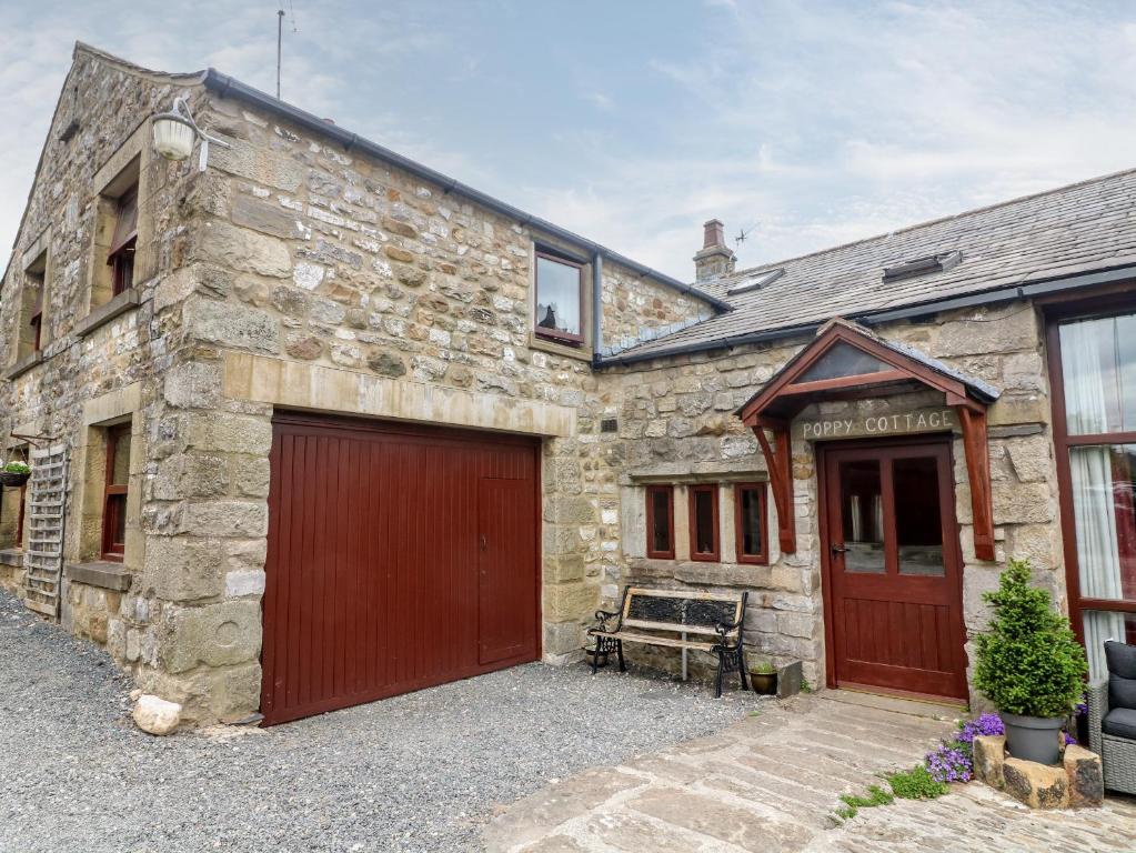 ein Steinhaus mit zwei Garagen und einer Garage in der Unterkunft Poppy Cottage in Settle