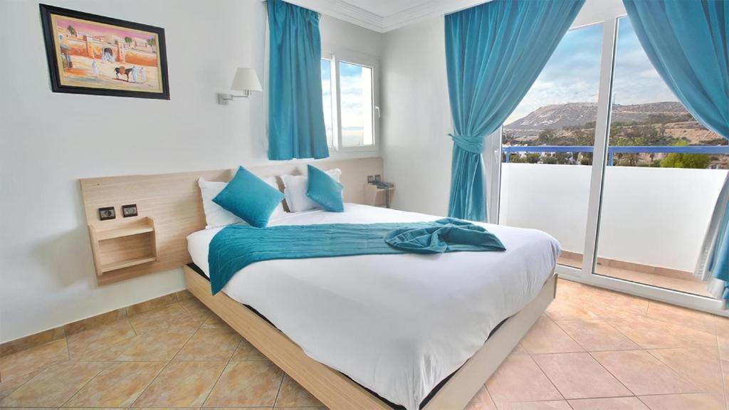 a bedroom with a large bed with blue curtains at Hotel Tildi Hotel & Spa in Agadir