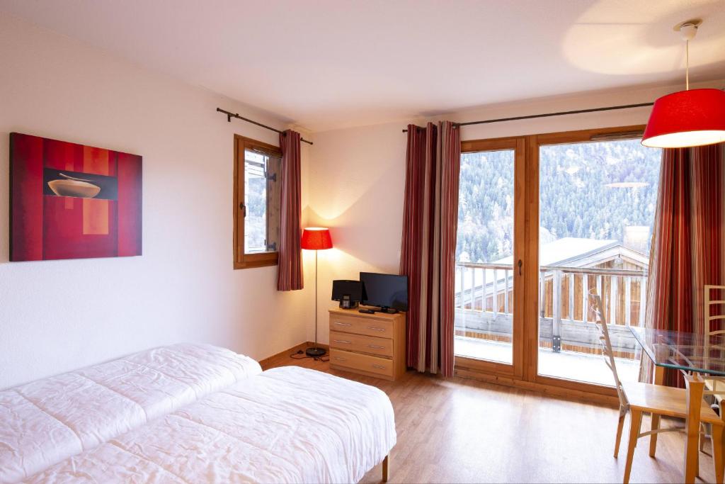 1 dormitorio con cama, TV y balcón en Le Hameau SPA & PISCINE studio 4pers by Alpvision Résidences, en Orelle