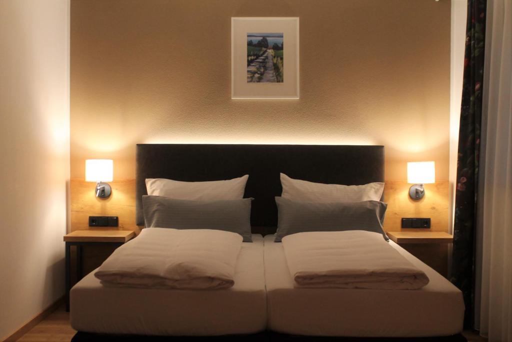 a bedroom with a bed with white pillows and two lights at Gasthaus Steidl in Bauerbach