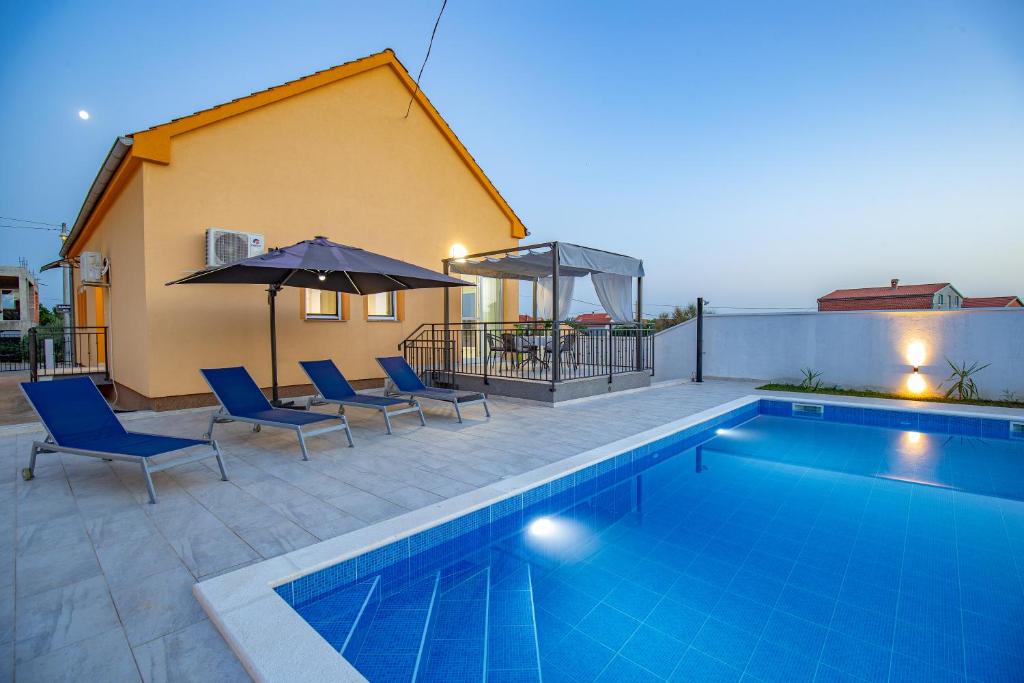una piscina con sillas y sombrillas junto a una casa en Villa Family and Friends private heated pool with jacuzzi, en Zadar
