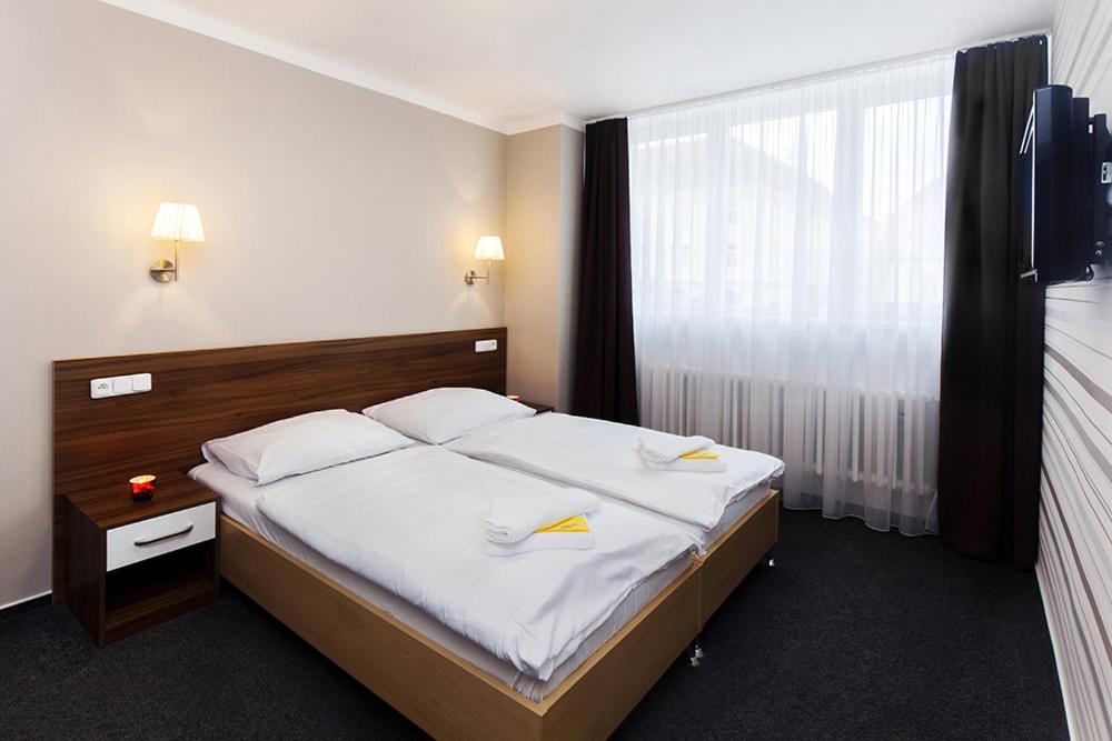 a hotel room with a bed with white sheets and a window at Arkada Hotel in Bučovice
