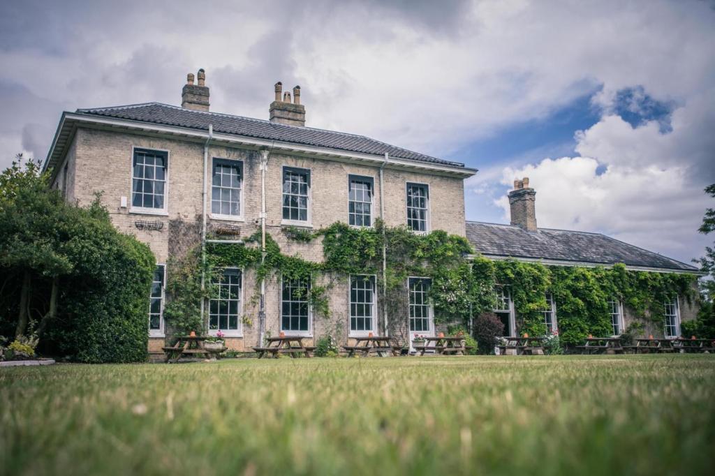 un gran edificio de piedra con un campo de césped delante de él en Caistor Hall en Norwich